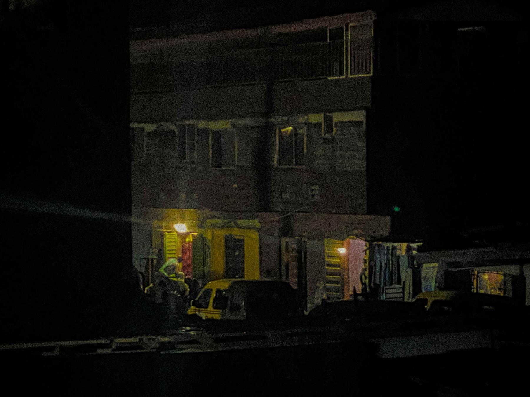 Lit doorways and a yellow bus in front of a dark building at night